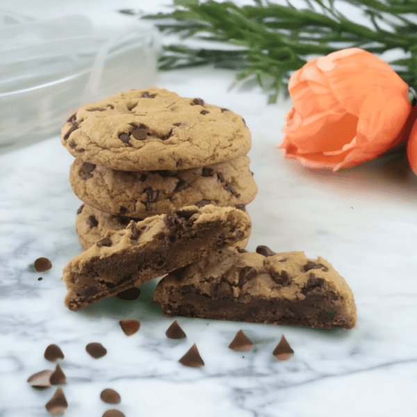 A cookie is sitting on the counter next to some flowers.