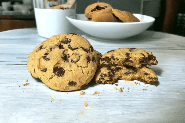 A table with two cookies and a bowl of chocolate chips.