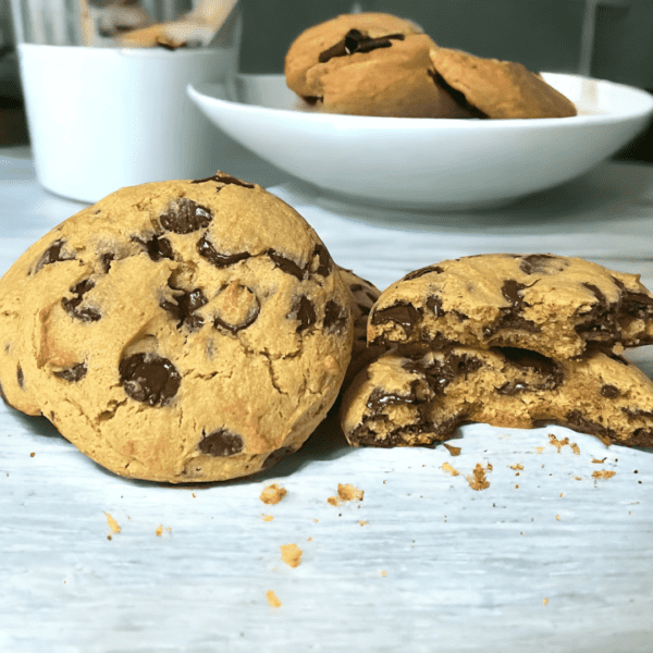 A table with two cookies and a bowl of chocolate chips.